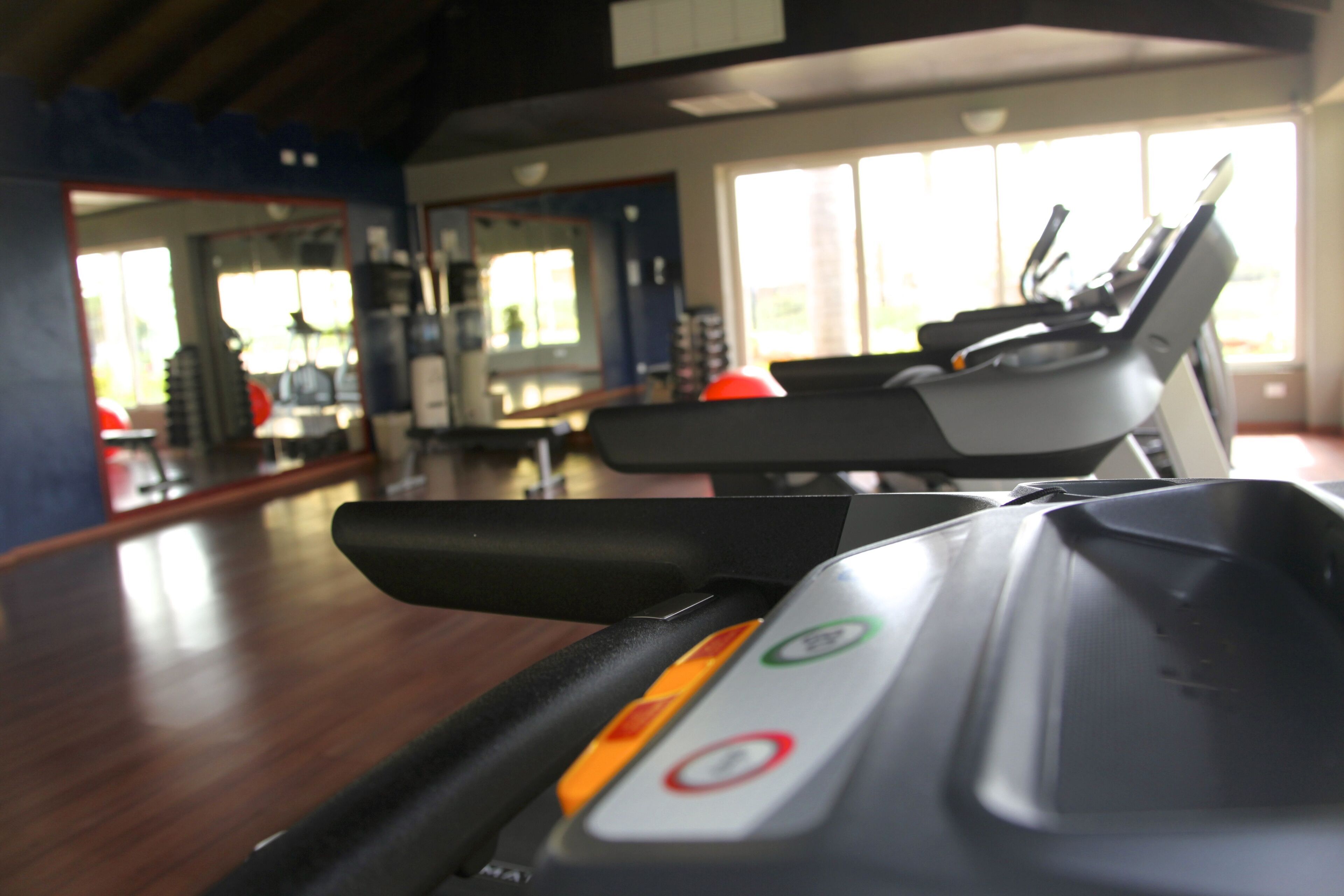 A treadmill in a gym with a wooden floor and a large mirror reflecting the room.