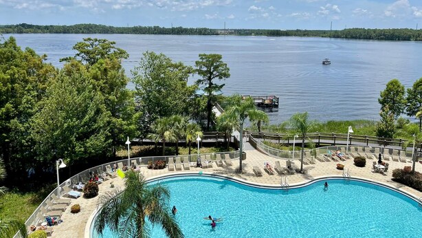 A swimming pool with a view of a lake, surrounded by lounge chairs and palm trees. - New! 1-King Bedroom, 2 baths with Breathtaking view at Blue Heron Beach Resort (Orlando)