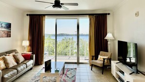 A living room with a sofa, armchair, TV, and a view of a lake through large sliding doors. - New! 1-King Bedroom, 2 baths with Breathtaking view at Blue Heron Beach Resort (Orlando)