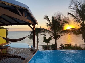 A pool with a view of the sunset over the ocean, surrounded by palm trees and a wooden deck. - Villa with exceptional sea view, infinity pool and jacuzzi, direct sea access (POINTE NOIRE)