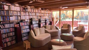 Una biblioteca con estanterías, muebles de mimbre y un ventilador de techo.