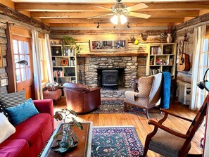 Cozy living room with a stone fireplace, comfortable seating area, and a bookshelf filled with books.