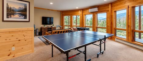 A room with a ping pong table, a TV, and a large window with a mountain view.