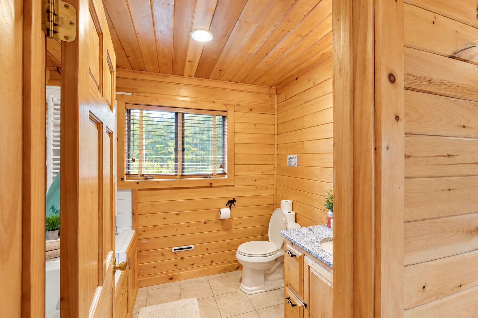 A wooden-paneled bathroom with a toilet, sink, and window.