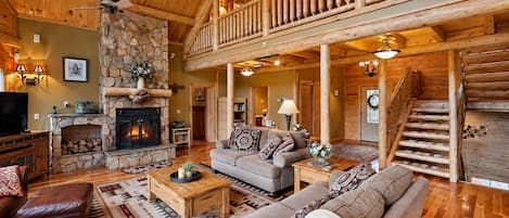 Una sala de estar amplia con chimenea de piedra, techo de madera y un balcón con vistas al interior.