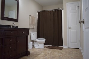 Un baño con tocador de madera oscura, inodoro blanco, cortina de ducha marrón y puerta blanca.