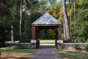 A gazebo with a brick roof and stone walls, surrounded by trees and a grassy area.