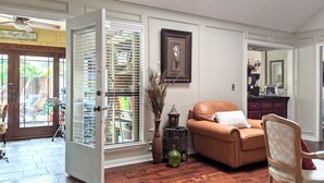 A room with a wooden floor, a brown leather sofa, a white chair, and a dining table. - Premier Secluded Oasis w/ Diving Pool, Hot Tub, Koi Pond & Outdoor Shower (Plano)