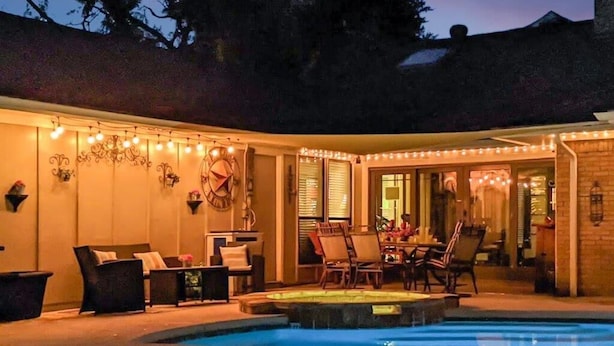 An outdoor pool area with lounge chairs and a hot tub, surrounded by string lights and a brick wall. - Premier Secluded Oasis w/ Diving Pool, Hot Tub, Koi Pond & Outdoor Shower (Plano)