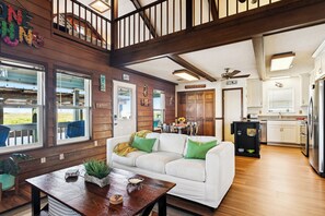 Un amplio salón con un sofá blanco, piso de madera y ventanas grandes.