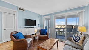 A living room with wicker furniture, a wooden coffee table, and a view of the balcony.