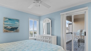 A bedroom with a bed, a dresser, a mirror, and a sliding door to a balcony with chairs.