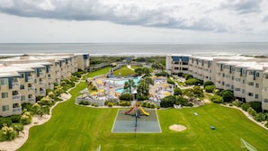 A resort with multiple buildings, a central pool area with slides, and a view of the ocean.