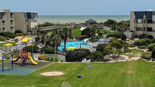 A resort with a swimming pool, playground, and a view of the ocean.