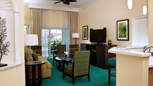 A hotel room with a living area, a dining area, a TV, and a kitchen.