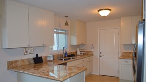 A kitchen with white cabinets, granite countertops, a stainless steel refrigerator, and a window with a curtain. - Sonoma Retreat w/ Pool, Spa & Spacious Yard – Near Wineries & Sonoma Plaza (Sonoma)