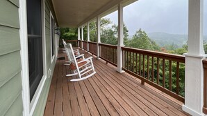 A covered porch with wooden railings and rocking chairs, overlooking a lush green landscape. - An Inspirational View.... (Horse Shoe)