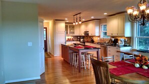 A modern kitchen with wooden flooring, white cabinets, a central island with stools, and a dining area with a red tablecloth. - An Inspirational View.... (Horse Shoe)