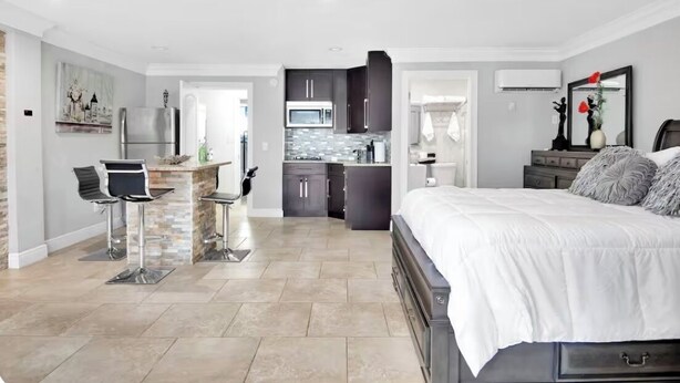 A modern bedroom with a large bed, a small kitchen area, and a dining area with two chairs.