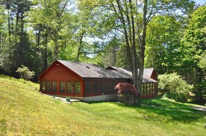 A red cabin with large windows, surrounded by lush greenery and trees.