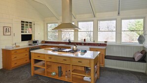 Tilava keittiö, jossa on suuri keittiösaareke, puukaapit ja ikkunoiden viereen rakennettu penkki.