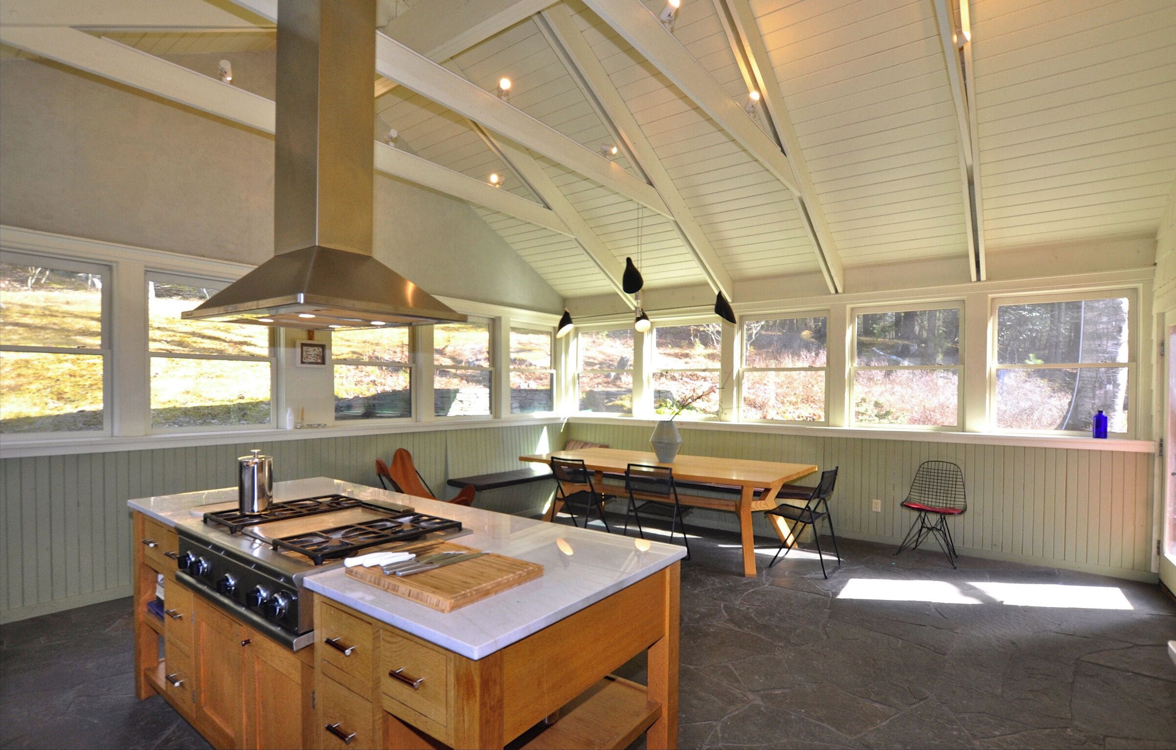 A kitchen with a central island, wooden cabinets, a stove, and a large window overlooking a natural landscape.