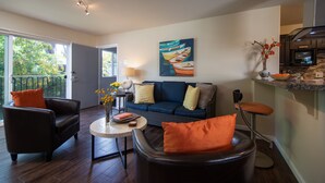 Een moderne woonkamer met een bank, stoelen, een bijzettafeltje en een keukenhoek met een magnetron.