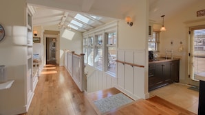A spacious hallway with wooden flooring, a staircase leading to a second floor, and a kitchen area with a sink and cabinets. - Pura Vida-Spring Special (Cambria)