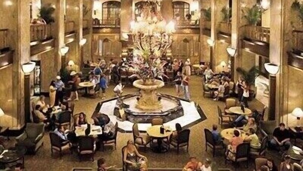 A spacious lobby with a central fountain, multiple seating areas, and a high ceiling with wooden beams.