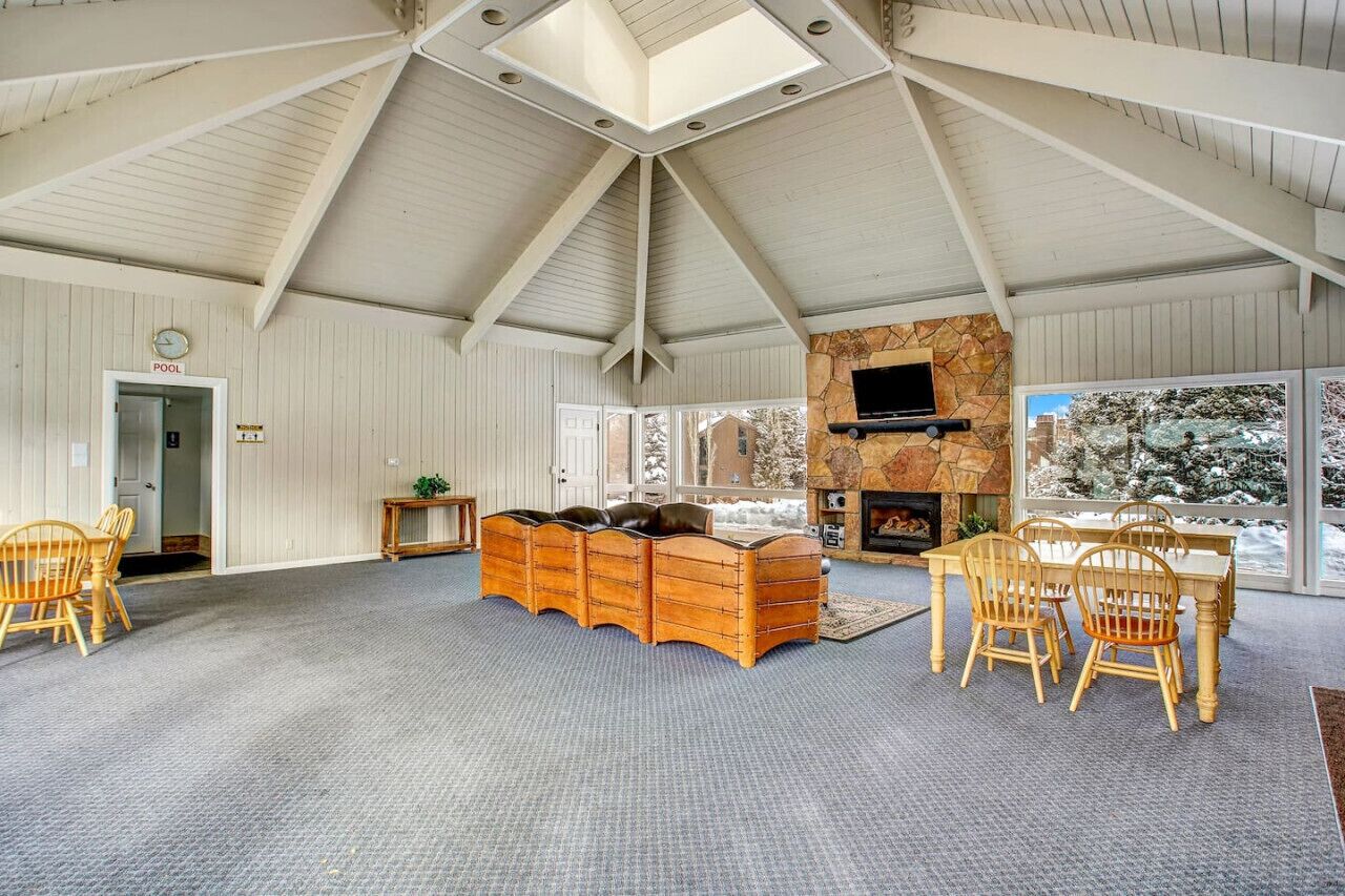 A spacious room with a high ceiling, a fireplace, a television, and a view of snow-covered trees.