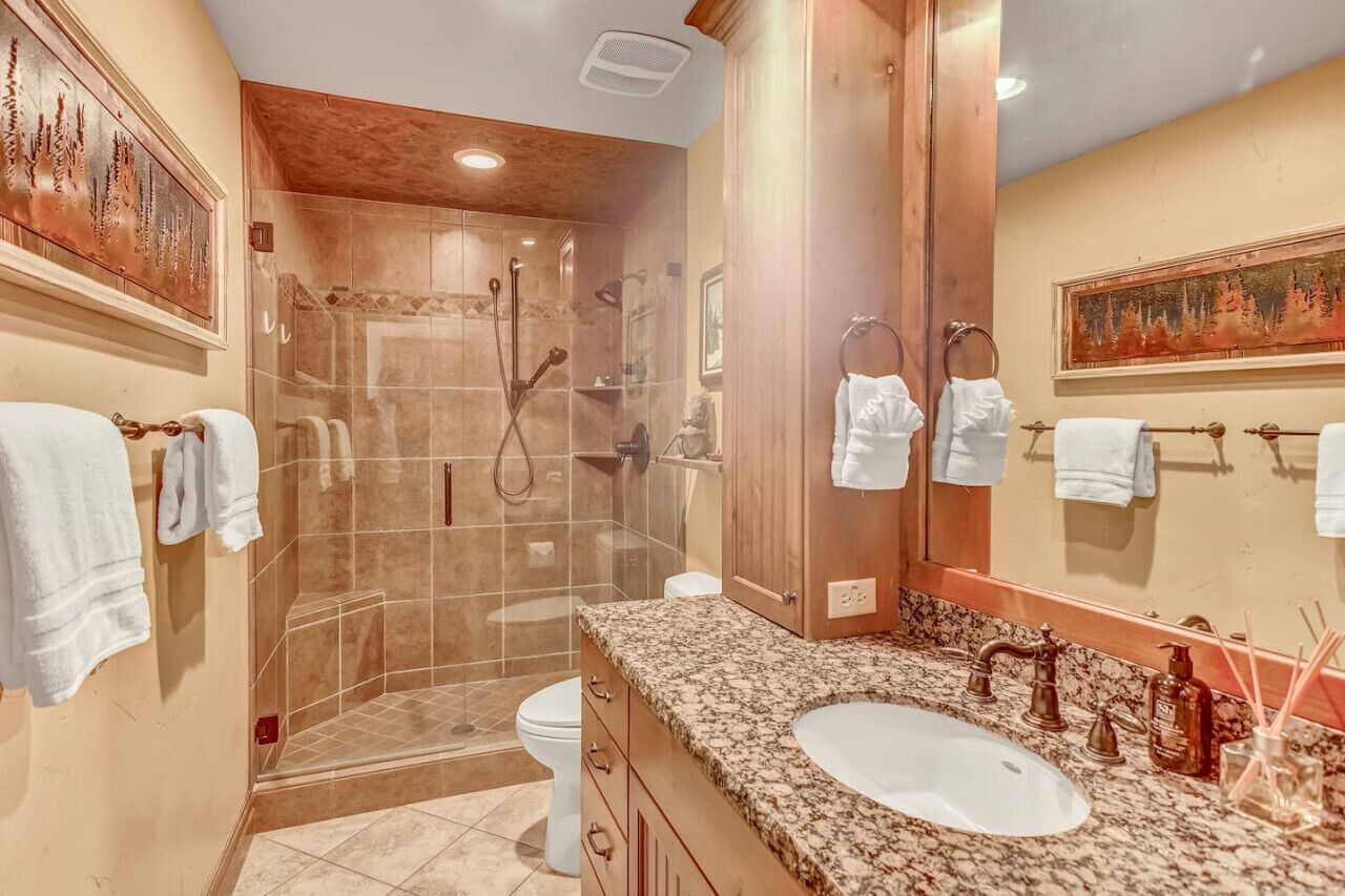 A modern bathroom with a glass-enclosed shower, a granite countertop sink, and wooden cabinetry.