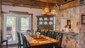 A dining area with a wooden table, black chairs, and a stone wall. There are hanging lights, a clock, and a sign above the door. - Private with large yard, community pool , fishing, game room, pets, easy access  (Sevierville)