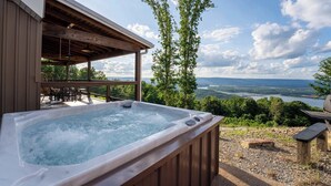 A hot tub with a wooden deck and a scenic view of a lake and mountains. - Mountain High Cabin with hot tub, fire pit, & indoor pool! (Bryant)