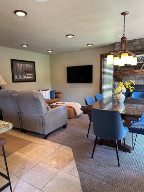 A living room with a gray sofa, blue chairs, a dining table, and a fireplace.