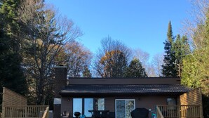 A wooden cabin with a deck, large windows, and a barbecue grill. - Muskoka, Cozy 2 Bedroom / 2 Bathroom Cottage located on the coveted Lake of Bay (Dwight)