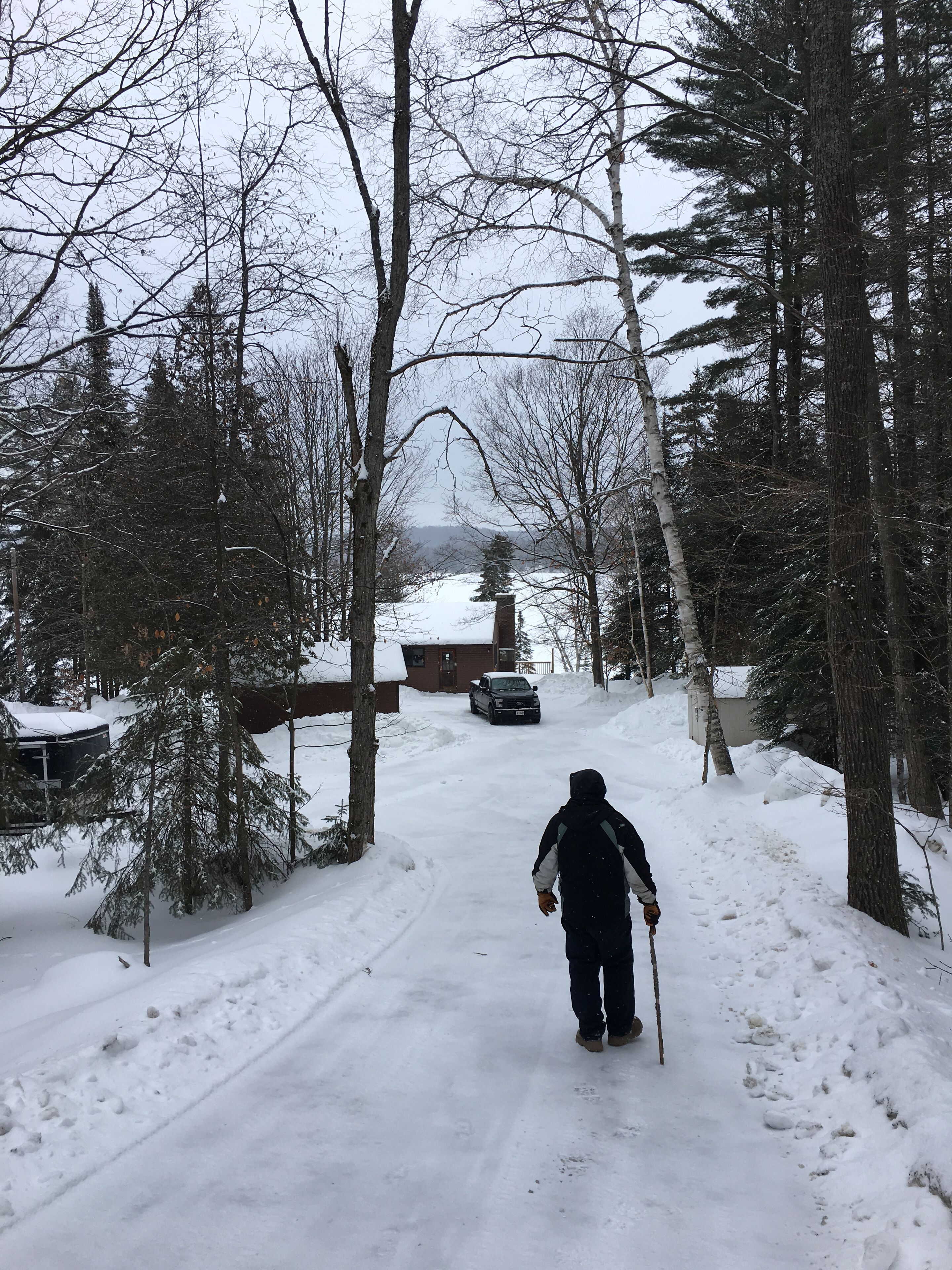 A snowy path leading through a forested area with a vehicle parked in the distance.