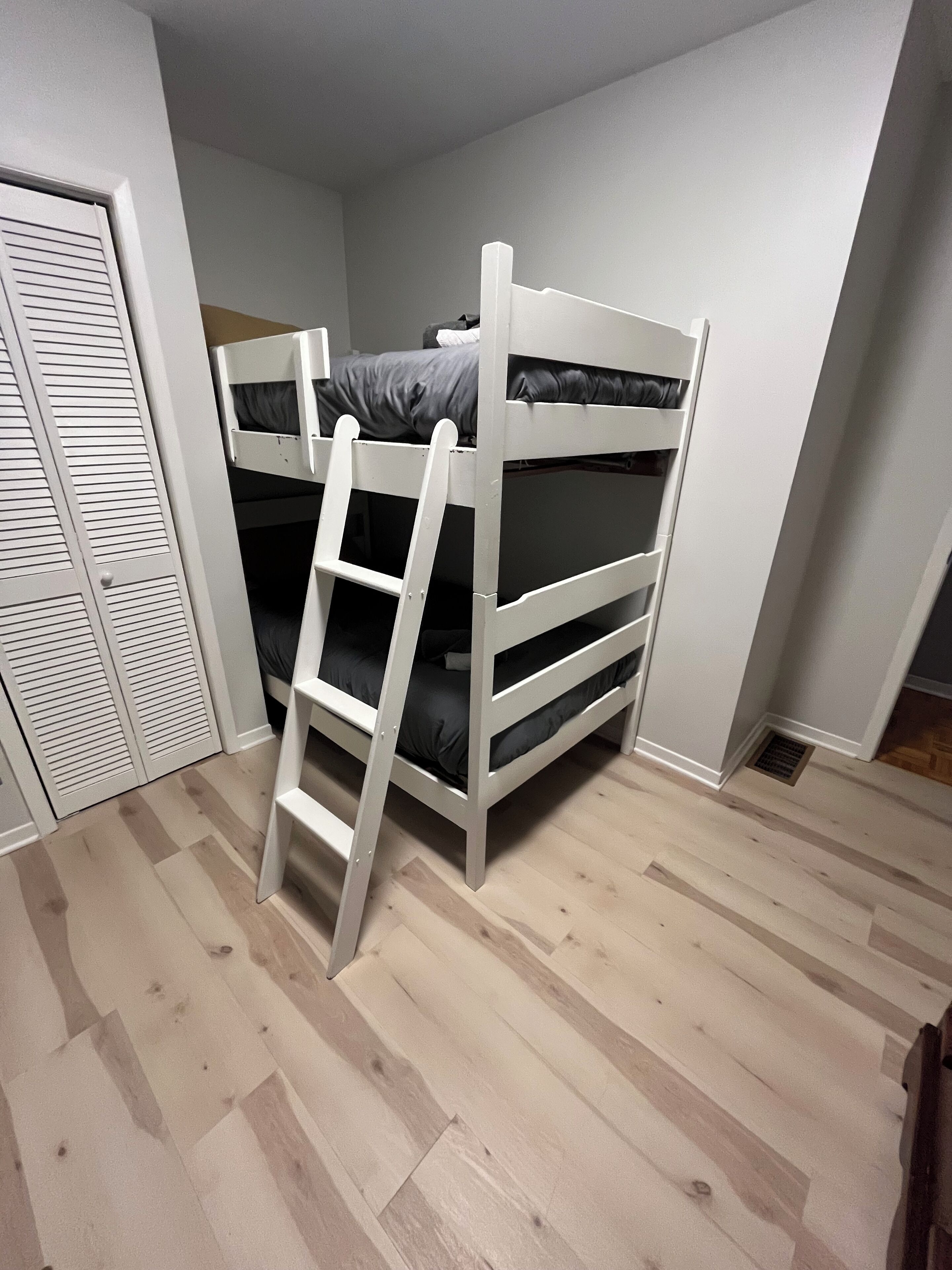 A bunk bed with a ladder, a wardrobe, and a wooden floor.