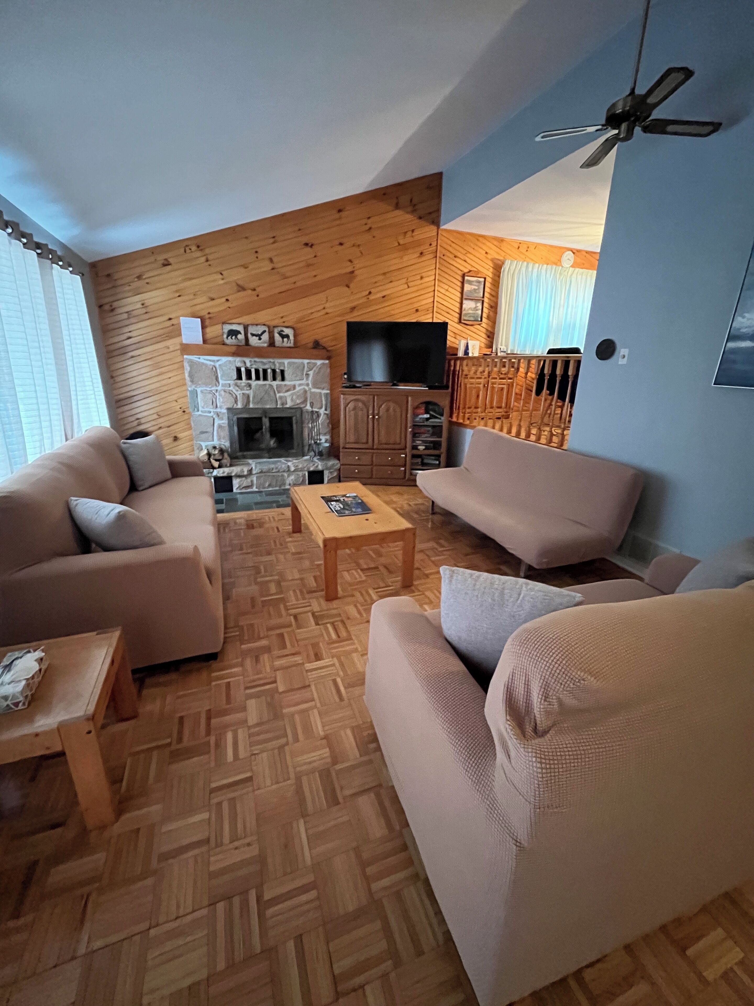 A living room with a stone fireplace, wooden walls, and a television.
