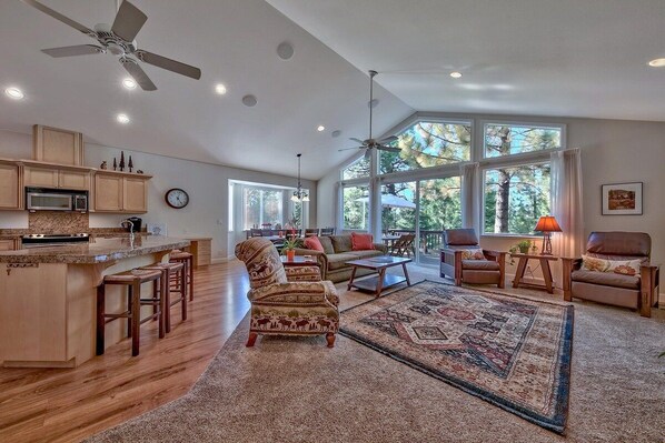 A spacious living area with a large window, a ceiling fan, and a kitchen with wooden cabinets and a microwave.