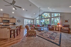 A spacious living area with a large window, a ceiling fan, and a kitchen with wooden cabinets and a microwave.