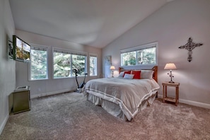 A bedroom with a large bed, two windows, a cross on the wall, and a treadmill.