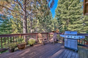 A deck with a grill, two Adirondack chairs, and potted plants.