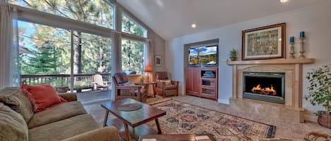 A spacious living room with a fireplace, large windows, and a ceiling fan.