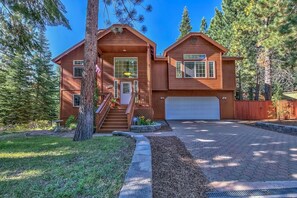 A two-story wooden house with a garage, surrounded by trees.