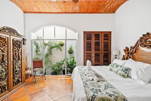 A bedroom with a bed, a chair, a wooden wardrobe, a window with plants, and a door with a wooden shutter. - Private Villa Downtown PV, 3 blocks to Beach, Private Pool, 360 rooftop views. (Puerto Vallarta)