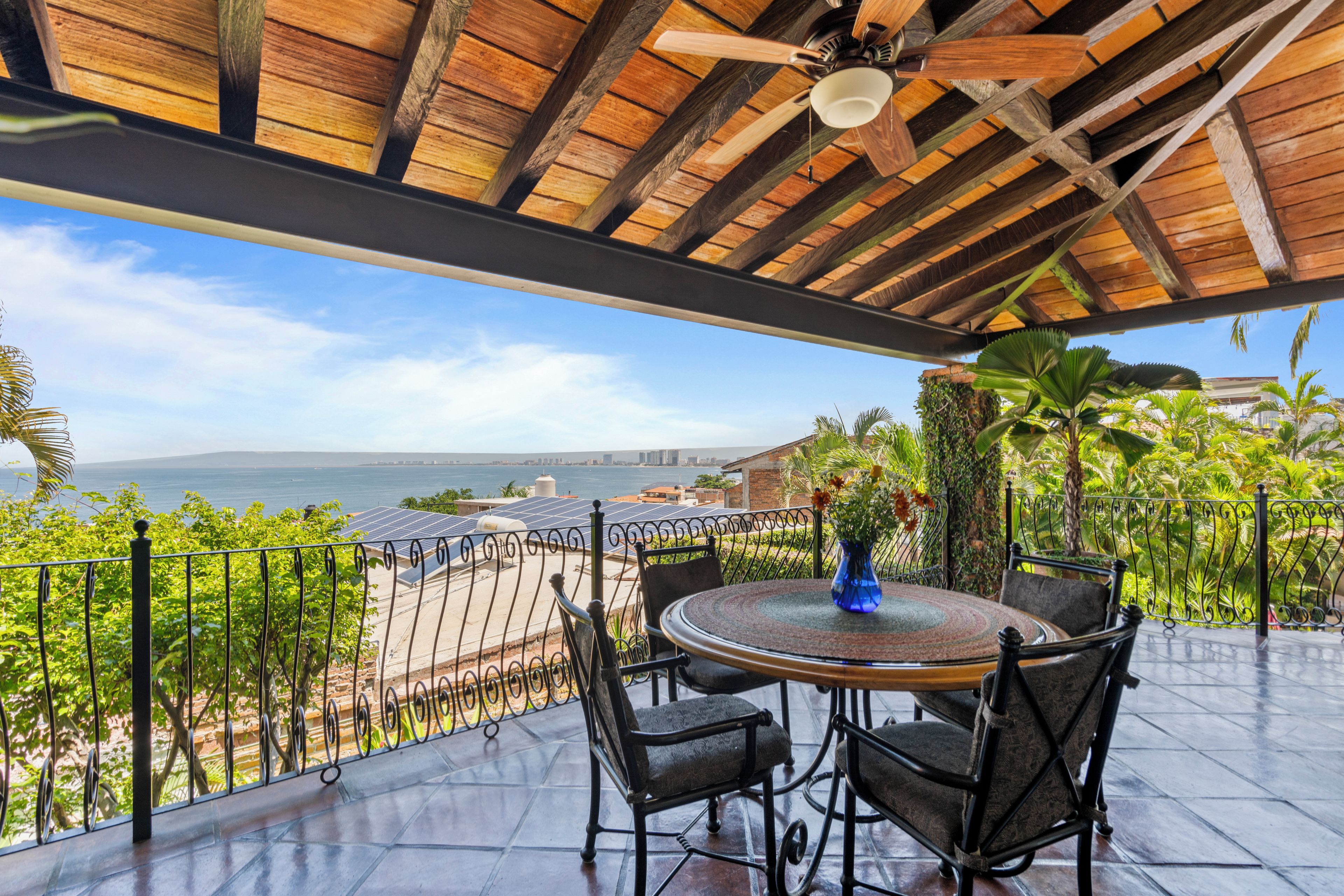 Un área de estar al aire libre techada con una mesa y sillas, con vistas panorámicas al océano y al horizonte de la ciudad.