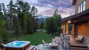 Een houten chalet met een jacuzzi, zitplaatsen buiten en een stenen open haard.