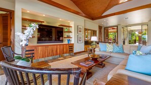A spacious living room with a wooden ceiling, a sofa set, a coffee table, and a dining area with chairs and a table.