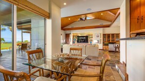 A spacious living area with a glass dining table, wooden chairs, and a kitchen in the background.
