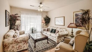 A living room with floral-patterned sofas, a glass coffee table, and a ceiling fan. - Historic Westside Home: Central Location, AC & Game Room (Colorado Springs)